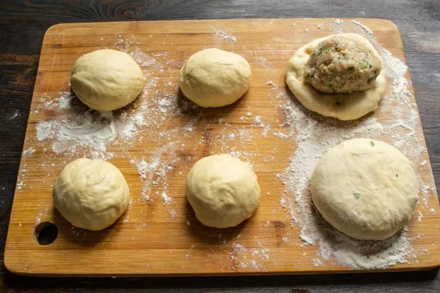 Лепим круглые булочки с начинкой из фарша. На этом этапе нужно плотно упаковать фрикадельку в фарш. Выкладываем заготовки на посыпанную мукой доску